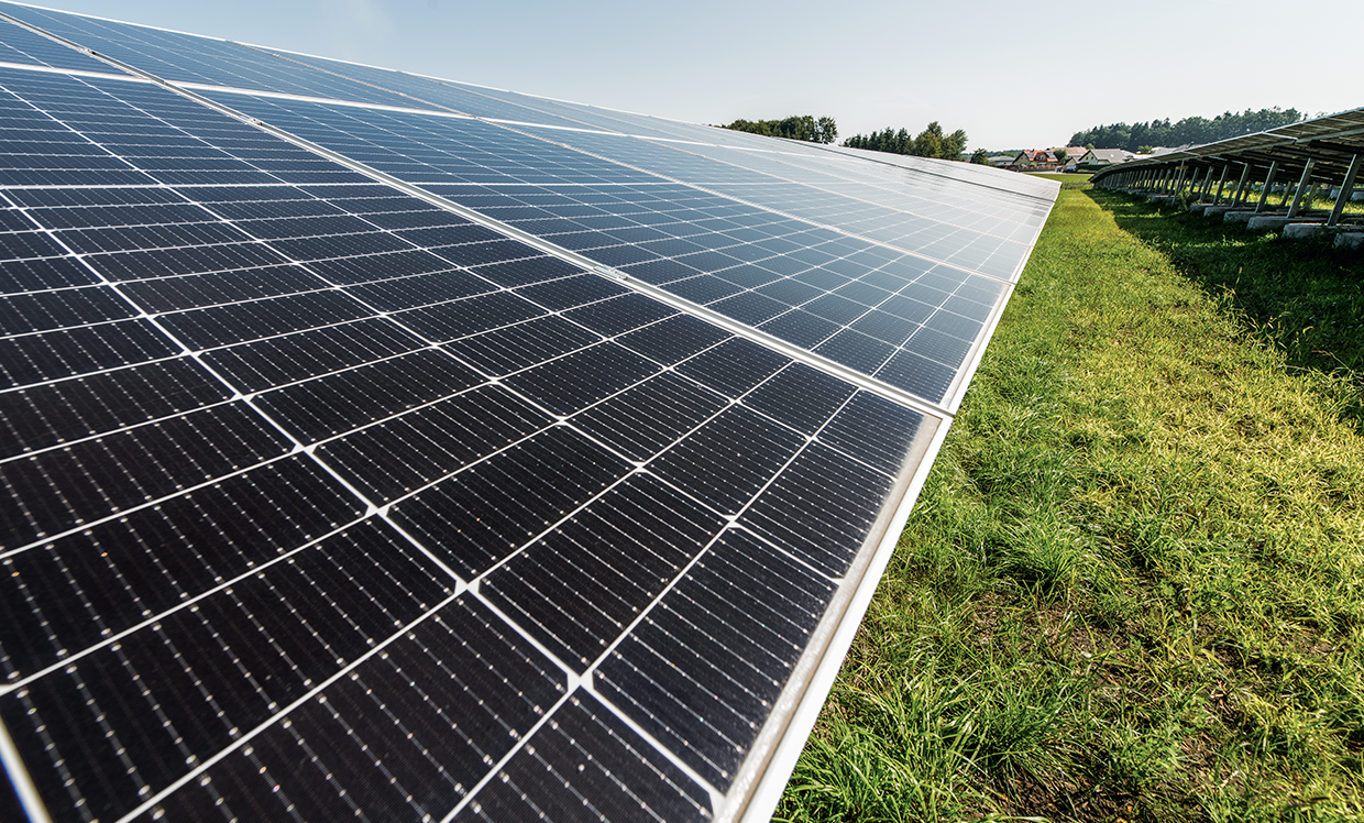 A close-up of a solar park featuring multiple solar panels arranged evenly on a green field. The panels are oriented towards generating renewable energy.